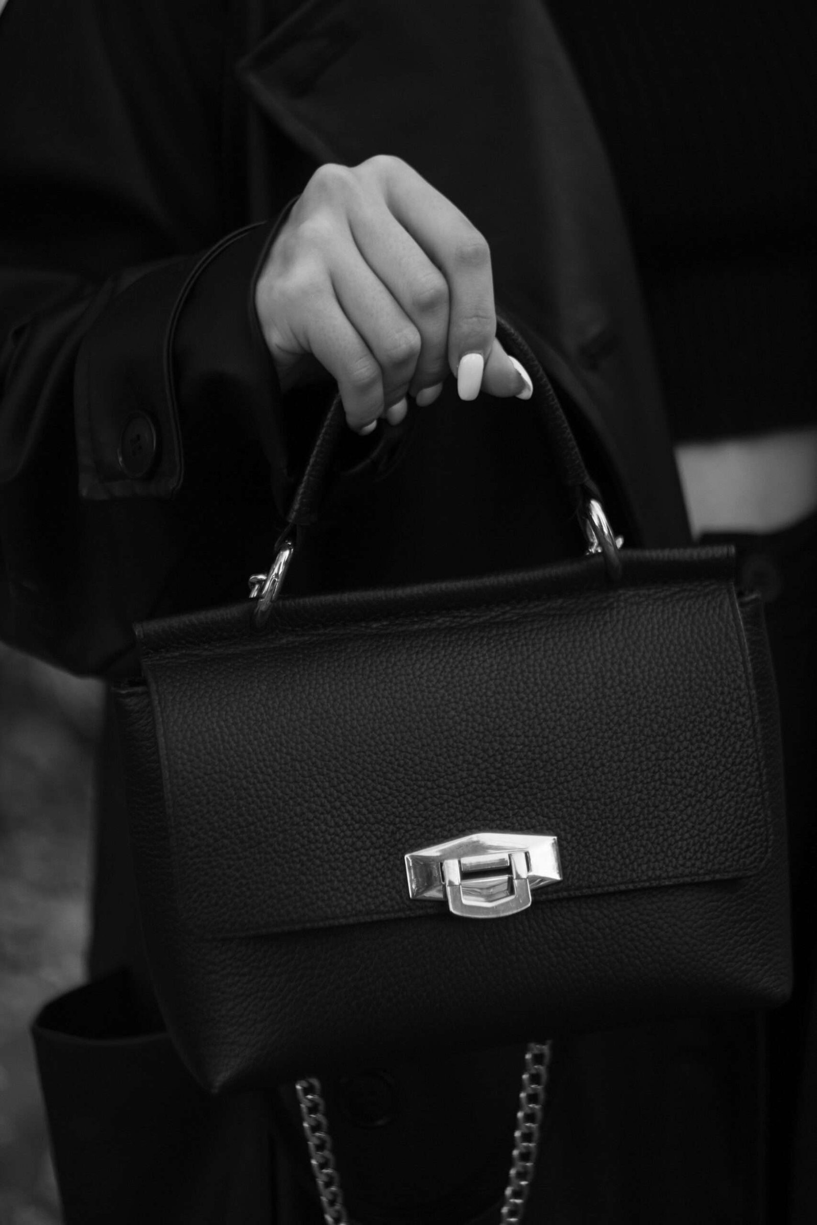 Elegant black handbag with human hand in a monochrome fashion-focused close-up.
