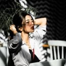 A fashionable woman in sunglasses poses with sunlight indoors, creating a chic and stylish vibe.
