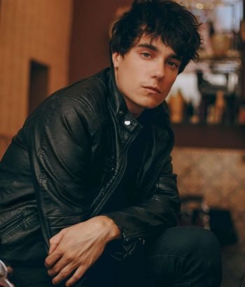 Stylish young man in a black leather jacket posing confidently indoors.