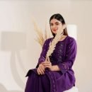 A stylish woman poses indoors wearing a purple embroidered dress, emanating elegance and modern fashion appeal.